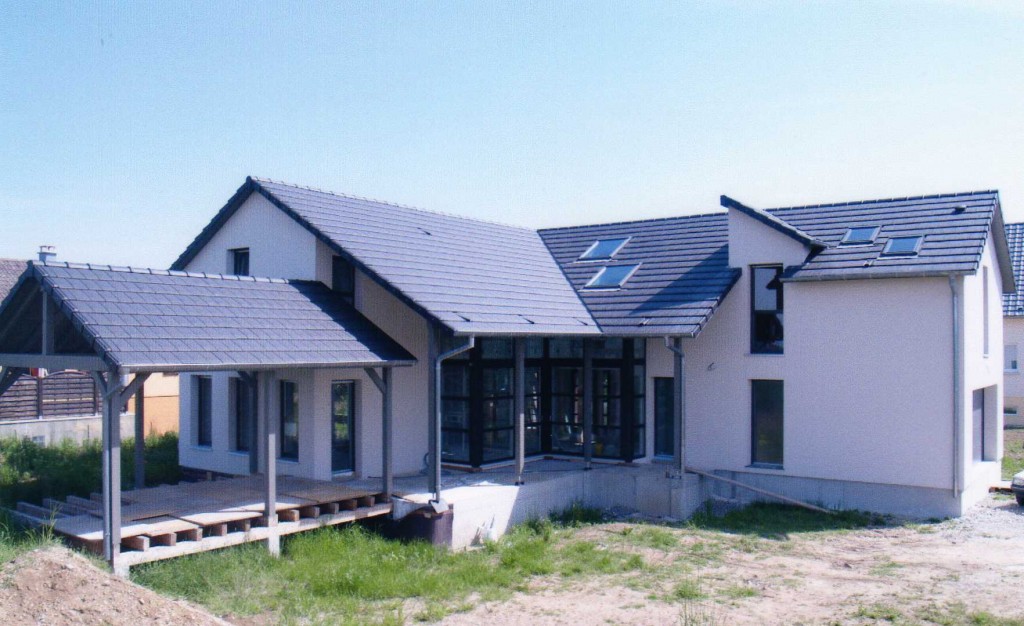 Maison en ossature bois avec grande baie vitrée et terrasse en bois.